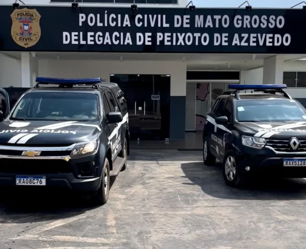 Foto da fachada da delegacia de Polícia Civil de Peixoto de Azevedo, duas viaturas pretas estão estacionadas na frente