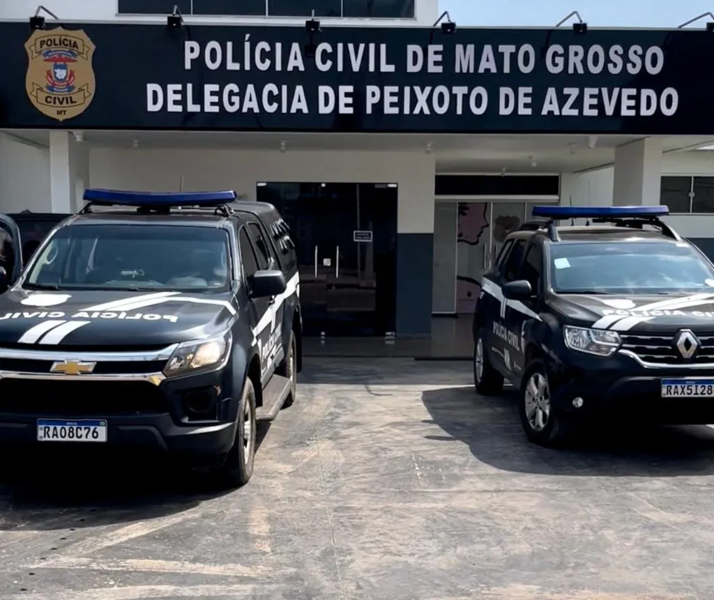 Foto da fachada da delegacia de Polícia Civil de Peixoto de Azevedo, duas viaturas pretas estão estacionadas na frente