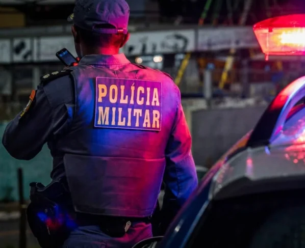 Policial militar ao lado de viatura com as luzes da sirene ligadas
