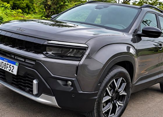 Jeep Avenger cinza estacionado em uma rua, visto de frente e pela lateral, com rodas pretas e detalhes prateados.